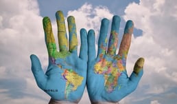 Mãos com o mapa do mundo desenhado nelas. Os continentes mostrados no mapa (América, Europa, África e Ásia) abrigam idiomas minoritários ou ameaçados de extinção.